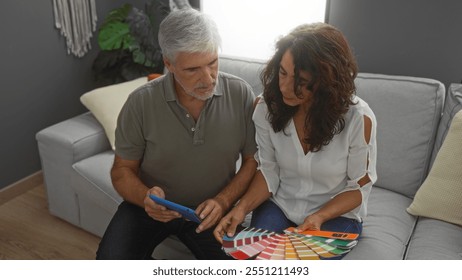 Middle-aged couple discussing color samples in a comfortable living room, woman holding swatches while man uses a tablet, suggesting home interior decision-making. - Powered by Shutterstock