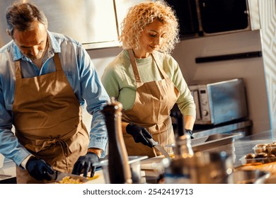 Middle-aged couple enjoying a cooking class with a chef preparing zucchini for a meal in the kitchen. - Powered by Shutterstock