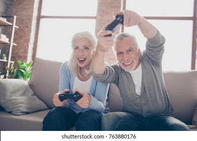 Middle-aged couple excited passionate about car racing game, sitting on a couch in their house in front of the tv screen playing with joysticks, very emotional