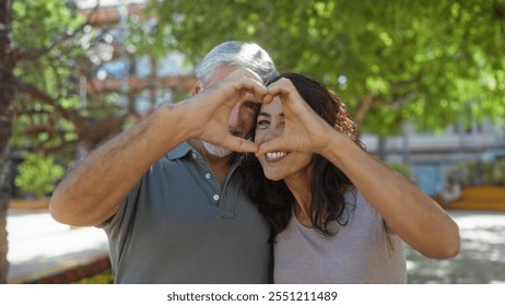 Middle-aged couple forms heart with hands sharing love in outdoor urban park setting with trees highlighting their togetherness and happiness. - Powered by Shutterstock