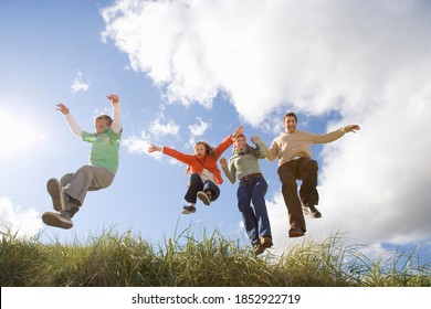 Middle-aged couple holding hands and jumping off a grass bank with their two children on a bright, sunny day out in the field