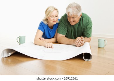 Middle-aged couple lying on floor looking at and discussing architectural blueprints together. - Powered by Shutterstock