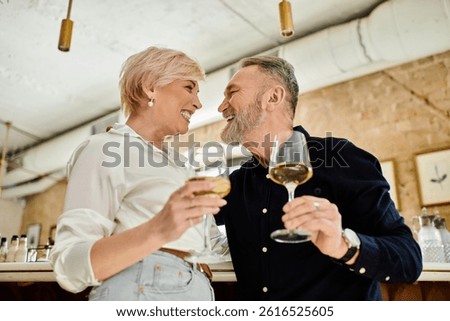A middle-aged couple smiles lovingly while raising glasses of wine in celebration.