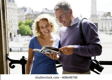 A middle-aged couple standing by Trafalgar Square, looking at a guidebook