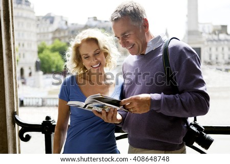 A middle-aged couple standing by Trafalgar Square, looking at a guidebook
