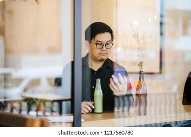 A middle-aged and educated looking Chinese Asian man is sitting in a cafe and texting on his smartphone during the day.  - Shutterstock ID 1217560780