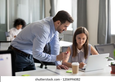 Middle-aged executive manager boss mentor teacher explaining online work to young focused intern looking at computer screen in office teaching training new worker instructing about software on laptop