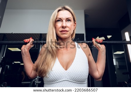 Middle-aged fitness woman doing squat exercise in a gym