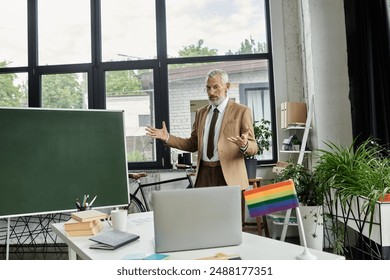 A middle-aged gay man with a beard teaches an online lesson in front of a laptop and a whiteboard, a rainbow flag is visible.