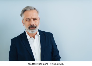 Middle-aged Grey-haired Man With Grey Beard, Looking At Camera. Half-length Front Bust Portrait On Plain Blue Background With Copy Space