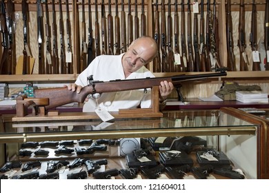 Middle-aged Gun Shop Owner Looking At Rifle In Store