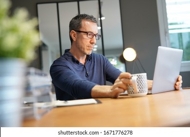 Middle-aged guy having hot drink, working on laptop