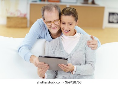 Middle-aged Happy Couple At Home Looking At Tablet