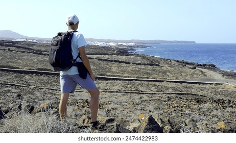 A middle-aged hiking tourist looks out at the fishing village from Lanzarote's lava coast. Active tourism concept - Powered by Shutterstock