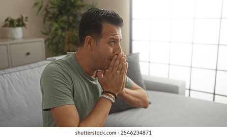 Middle-aged hispanic man contemplatively sits in a modern living room, highlighted by natural indoor light and minimalistic decor, suggesting a thoughtful or reflective moment. - Powered by Shutterstock