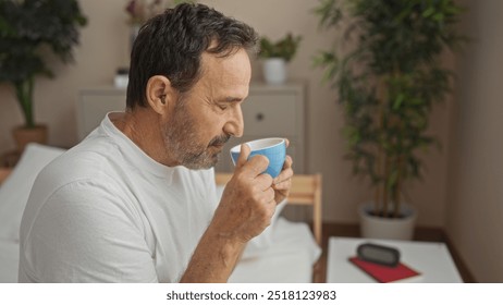 Middle-aged hispanic man drinking coffee in a cozy bedroom with plants and morning light streaming in. - Powered by Shutterstock