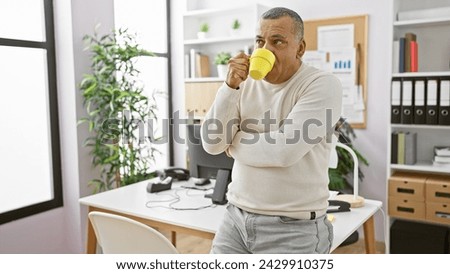 Middle-aged hispanic man drinking coffee in a modern office setting, reflecting a moment of relaxation during work.