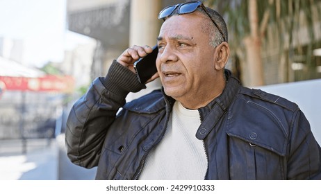 A middle-aged hispanic man in a leather jacket talking on a mobile phone on a city street. - Powered by Shutterstock