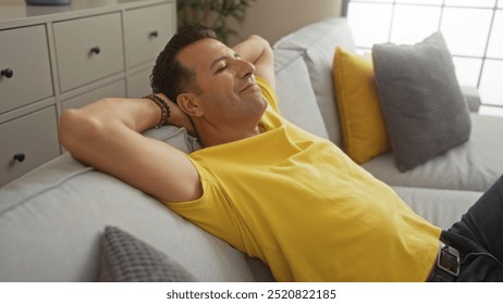 Middle-aged hispanic man relaxing on a sofa in a modern living room with bright yellow and grey pillows in an apartment interior - Powered by Shutterstock