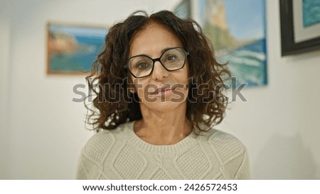 Middle-aged hispanic woman with glasses posing in art gallery
