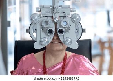 Middle-aged Indian or Nepali woman looking through Optical Phoropter during eye exam, diagnostic ophthalmology  - Powered by Shutterstock