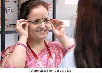 Middle-aged Indian or Nepali woman trying on new eyeglasses, recommended by experts, at optical shop