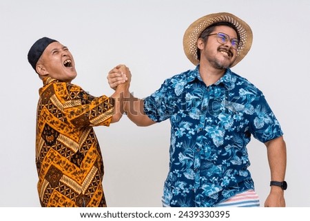 A middle-aged Indonesian man in batik and kopiah in a playful arm wrestling bout with a tourist in a hawaiian shirt, both isolated on white.