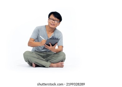 A Middle-aged Korean Man Reflective Vest Sitting On A Floor With Legs Crossed, Holding A Digital Tablet And Looking Away. Full Length Studio Shot Isolated On White Background.