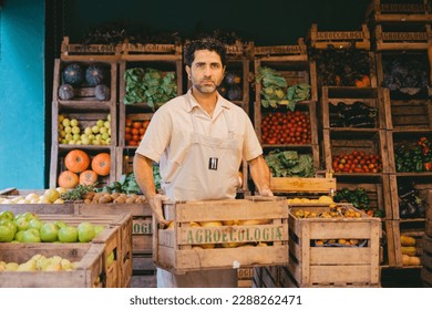 Middle-aged latin grocer's carrier unloading a crate of lemons while looking at the camera.