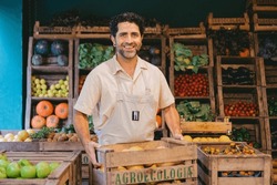 Middle-aged Latin Man Smiling With A Crate Of Pumpkins In A Vegetable Store While Looking At The Camera.