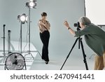 A middle-aged lesbian couple in a photo studio. One woman, a photographer, captures the other, a model, in front of a fan.