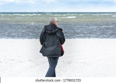 A Middle-aged Man, 50 Plus, Walks Along A White Beach. Outdoor Activities That Include Social Distance Is Safe Activities During The Coronavirus Pandemic. Blue Sky, Turquoise Water In The Background