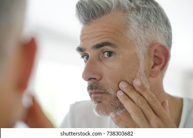 Middle-aged man applying cosmetic on his face, mirror view