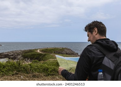 Middle-aged man with backpack consulting a map outdoors with the sea in the background. Concept of tourism and travel