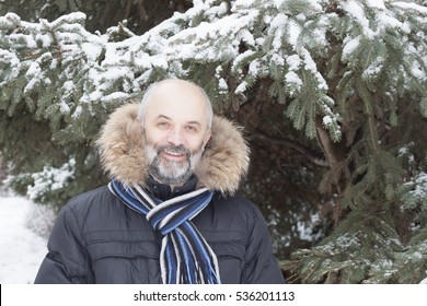 Middle-aged man with a beard in a jacket with fur hood. Scarf Milan host, fir trees covered with snow