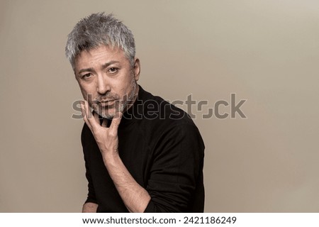 A middle-aged man with a beard is touching his chin.