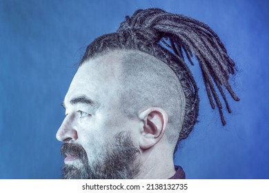 A middle-aged man with a beard and an unusual hairstyle. Artificial dreadlocks. Challenging appearance. Adult male with mohawk and dreadlocks in profile.