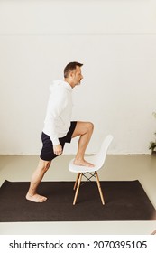 Middle-aged Man Doing Step Up Stretch Exercises Using A Chair During His Daily Workout At Home During The Covid-19 Pandemic