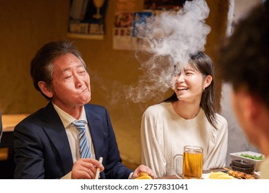 A middle-aged man drinking alcohol while smoking a cigarette at an izakaya
