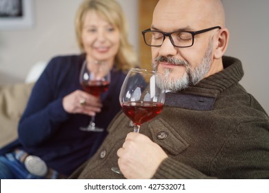 Middle-aged Man Enjoying A Glass Of Red Wine Sniffing The Bouquet With His Eyes Closed In Bliss Watched By His Wife Alongside Him