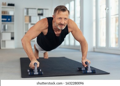 Middle-aged Man Exercising On Handles For Push-ups On Black Mat In Office, Viewed From His Face