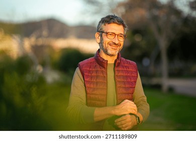 Middle-aged man with glasses smiling while standing in a park during golden hour