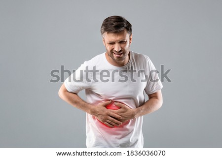 Middle-aged man holding his lightened with red right side, suffering from liver pain, grey studio background, copy space. Sad man having hepatitis, rubbing his right side. Liver diseases concept