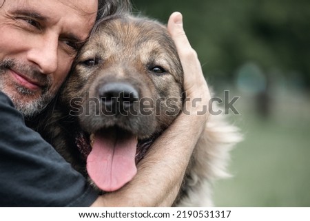 A middle-aged man hugs a dog on a walk. Close-up.