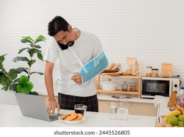 Middle-aged man injured with sling engages in a serious phone conversation while using laptop insurance premium claim, worker suggests shifting to a work-from-home setting cause accident arm broken. - Powered by Shutterstock