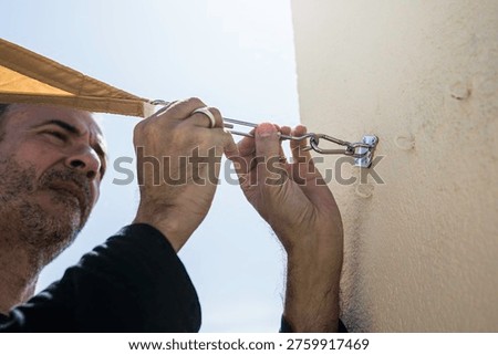 Middle-aged man installing a sail shade on a building's terrace.
DIY, lifestyle, people, home life