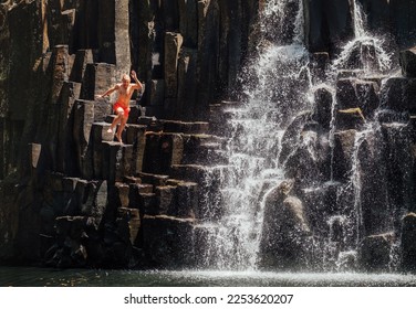 Middle-aged man jumping in waterfall lake. Falling water streams flow on black volcanic stone cascades. Rochester Falls waterfall - popular tourist spot in Savanne district in Mauritius. - Powered by Shutterstock