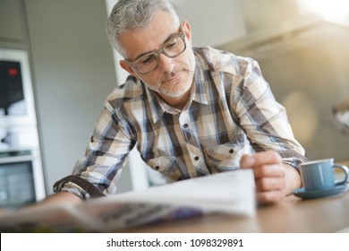 Middle-aged man in kitchen reading newspaper - Powered by Shutterstock