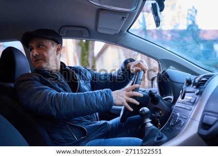 Middle-aged man looking back while reversing car with hands on steering wheel in residential area