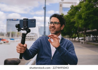 Middle-aged man making a video call through a cell phone held by a gimbal with the city blurred in the background.
